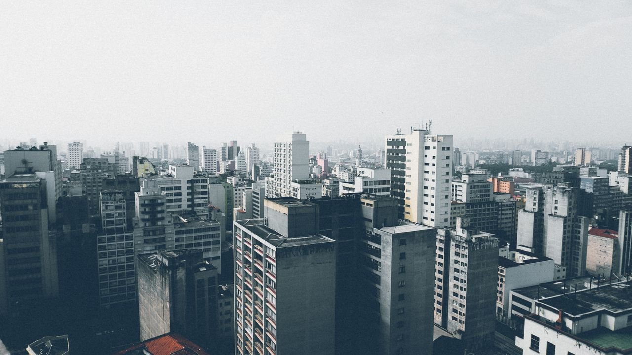 Home Aerial view of a dense urban cityscape with numerous skyscrapers and high-rise buildings under a cloudy sky.